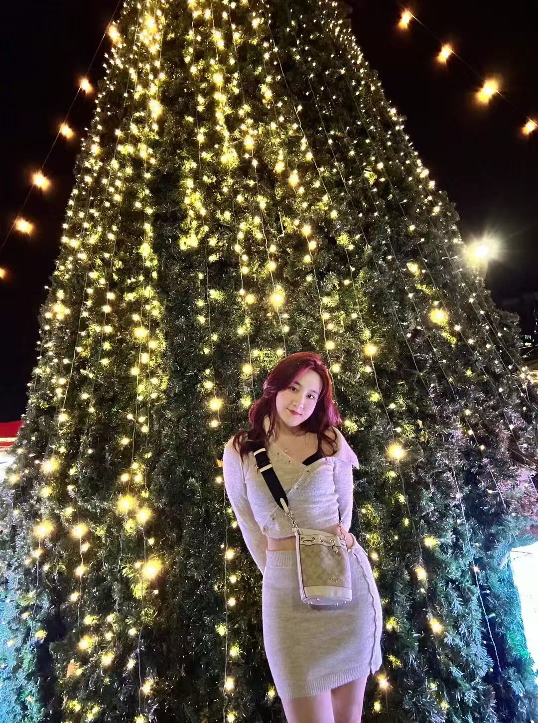 Portrait of Chelsea Yu standing in front of a Christmas tree lit with warm lights